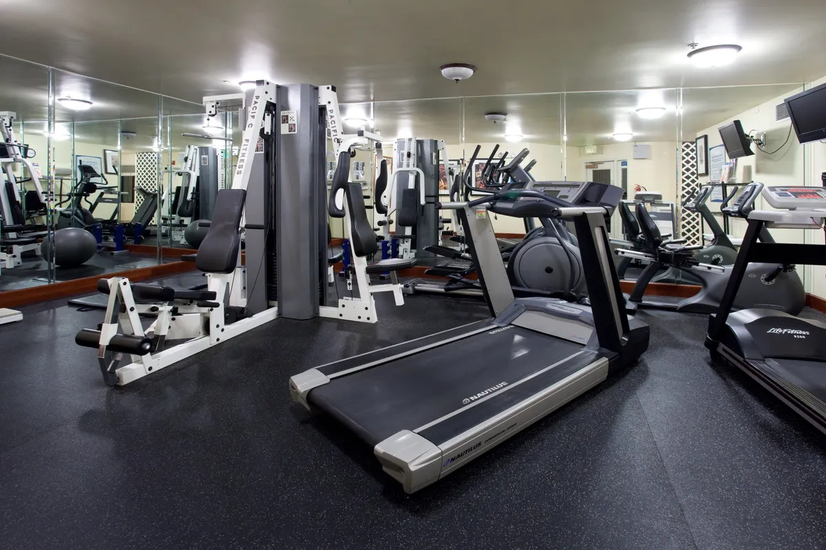 An interior shot of a well-equipped fitness center featuring treadmills, weight machines, and exercise bikes. The space is bright and inviting, designed for maintaining an active lifestyle and supporting both individual workouts and group classes.