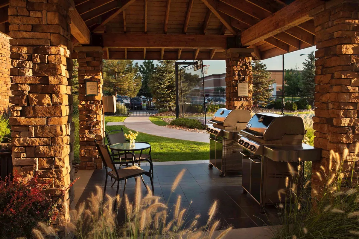 A landscaped outdoor area featuring grill stations, stone pillars, and comfortable outdoor seating. The space is designed for socializing, relaxation, and enjoying nature, with pathways that invite guests to unwind or gather after a productive day.