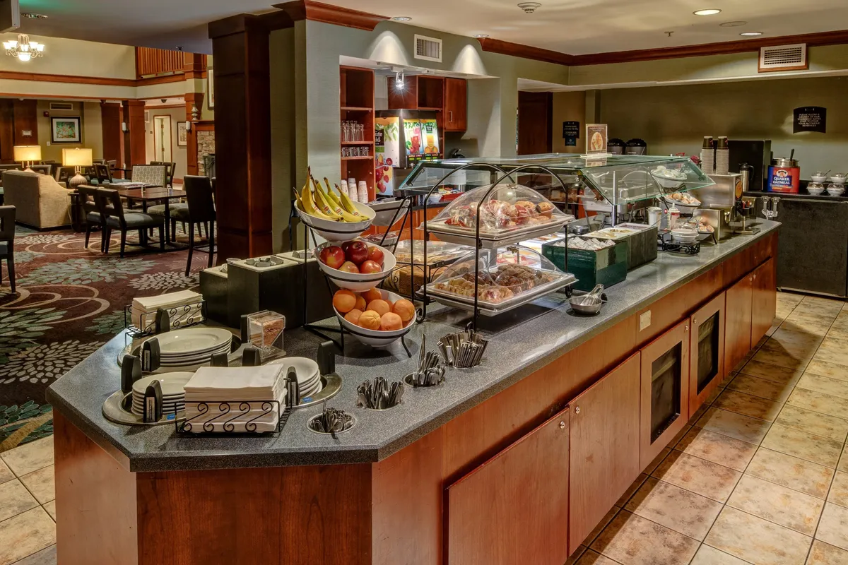 A cozy dining area is shown here, featuring a breakfast display, a fruit basket, and a well-stocked coffee station. The table setup hints at casual dining and opportunities for guests to socialize over meals, complementing the living space's versatility for both leisure and productivity.