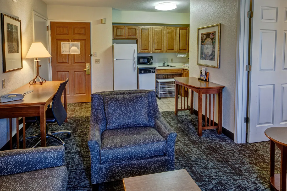 The image showcases a warm interior with a comfortable seating area, a well-equipped kitchenette, stylish wooden furniture, and tasteful artwork. The space is designed for relaxation, socializing, cooking, and even working, offering an inviting atmosphere that balances coziness with practicality.